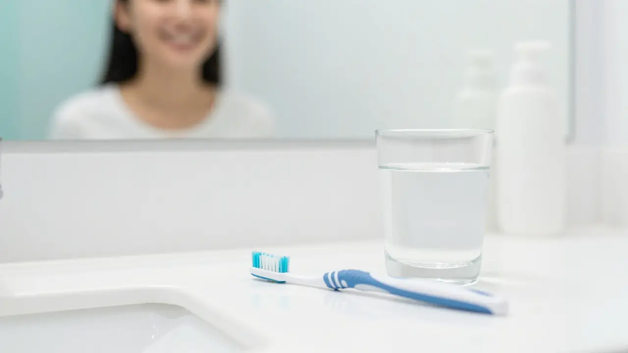 Zubní kartáček a mezizubní kístky na bílém pultu v koupelně.